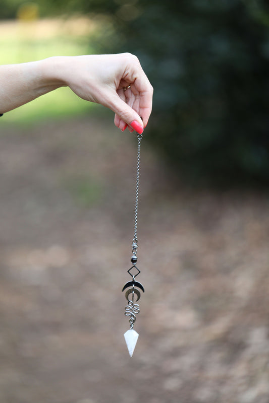 Mano sujetando un péndulo de cristal al aire libre