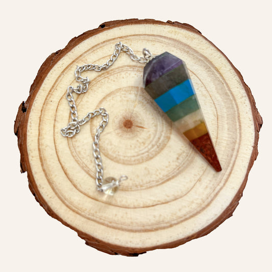 Péndulo de 7 chakras con piedras naturales y cadena plateada sobre rodaja de madera