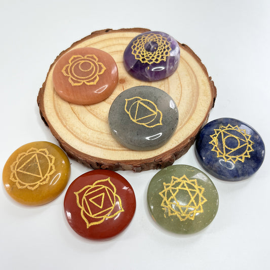 Kit de 7 piedras de los chakras sobre una rodaja de madera, con los símbolos grabados en dorado